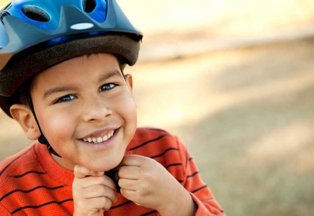 Young boy smiling as he puts on a bike helmet